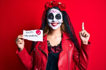 Woman wearing day of the dead costume holding happy halloween paper surprised with an idea or question pointing finger with happy face, number one