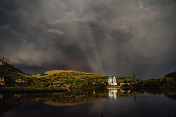 Fototapeta na wymiar white Church on the lake, the sun's rays Shine through the clouds, evening landscape