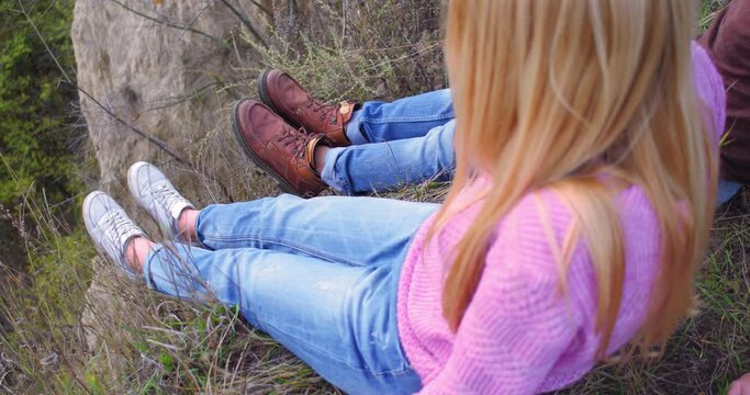 Young couple sits on cliff mountain on walk through forest. Sitting on grass they look at each other and have fun. High quality 4k footage