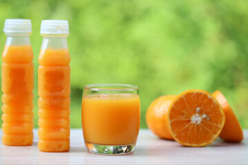 Glass of orange juice and oranges on natural green background