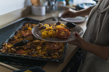Unrecognizable Caucasian woman plating baked rice in the kitchen of the house. Typical recipe from Spain.