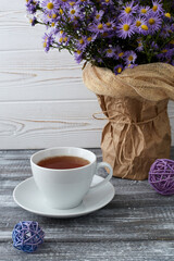 Romantic background with a cup of tea, lilac flowers in a vase on a gray wooden table