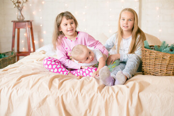 Cute sisters and little brother  in pajamas have fun in in a Scandinavian style bedroom decorated with Christmas garlands and needles on a large bright bed. Christmas mood. Christmas mood. Family time