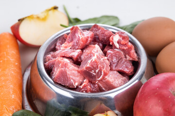 Closeup on barf raw meat chunk food for dog surrounded with other ingredients of vegetables and egg