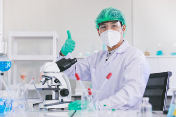 Portrait of young Asia male scientist wearing face mask and safety glasses thumbs up with equipment inside a laboratory.