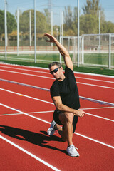 Mature fitness man with glasses stretching on the red running track. Lifestyle and sports