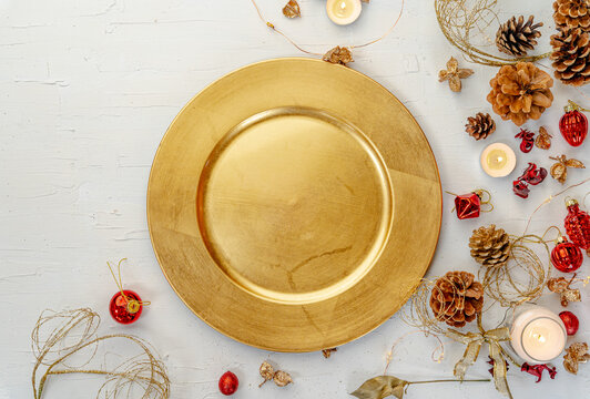 Overhead shot of a golden plate with rustic colorful Christmas decors on white wooden table