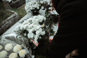 A women putting flowers on a grave on All soul's day in a vblack coat.