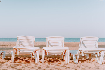 A row of three sun loungers with sea views. Sunny beach with three sun loungers. On a Sunny summer vacation. horizontal image.Beach chairs by the sea in neutral colors.