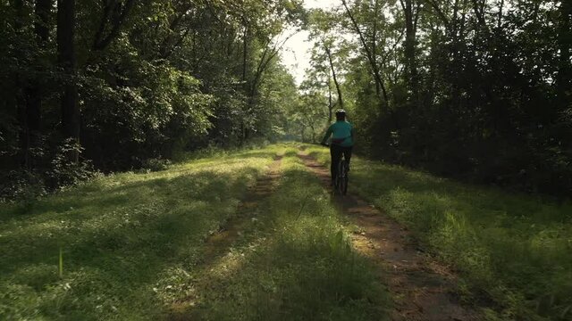 Woman riding mountain bike down wooded dirt path, Tracking Shot, Slow Motion