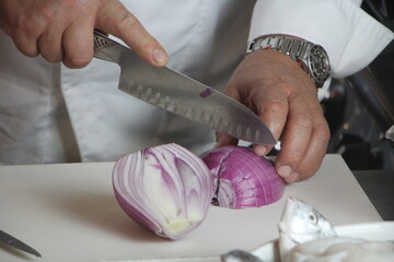 Cuoco taglia cipolla rossa di Tropea su tagliere. Cucina professionale.