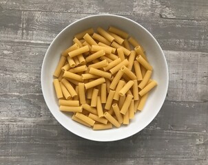 A bowl of tortiglioni pasta against a wooden background 