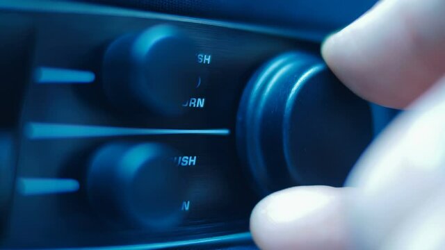 The hand turns and presses the knob on the front panel of the black stereo  equipment. Closeup