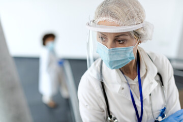 Distraught female doctor wearing visor and protective face mask due to coronavirus pandemic.