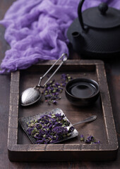Obraz na płótnie Canvas Blue mallow flowers tea in steel plate with vintage strainer infuser in wooden box with black iron cup and teapot with purple cloth