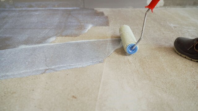 Concrete floor priming is the final preparatory stage for surface strengthening. Priming the concrete floor with a long handle roller. Floor priming process.