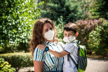 Schoolboy is ready go to school. Mother puts a safety mask on her son's face. Cute boy with a backpack outdoors. Back to school concept. Medical mask to prevent coronavirus. Coronavirus quarantine