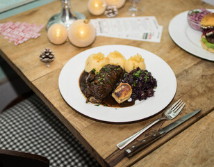 Rinderroulade an weihnachtlich gedecktem Tisch mit Tannenzapfen und gold glitzernden Christbaumkugeln auf Holztisch