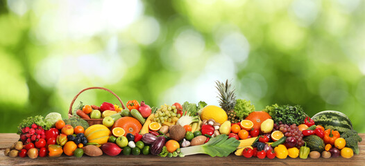 Assortment of fresh organic vegetables and fruits on wooden table against blurred green background. Banner design