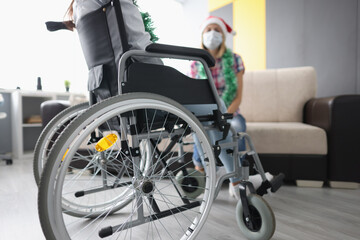 Man sits in a wheelchair in front of woman in santa claus hat and New Year's garland. New Year and Christmas celebration concept