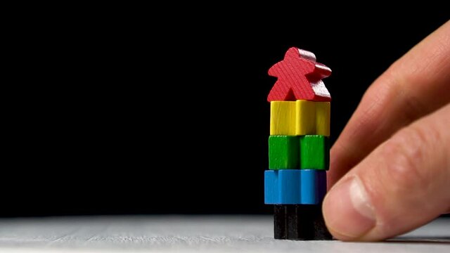 Crash of the figurine tower after pulling out the basic fundamental block. Colored shapes on a black background. Conceptual miniature of a business and career crash