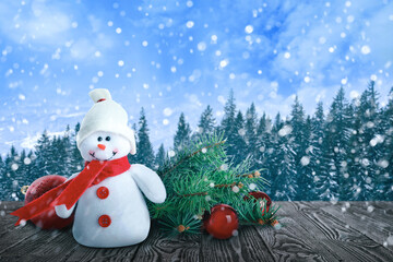 Cute toy snowman with fir tree branch and Christmas balls on wooden table in winter forest