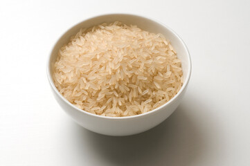 Cup filled with raw rice grains, on white background and shadow
