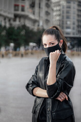 Young woman with black mask enjoying the sun in the middle of the city. Pandemic coronavirus. Empty city and model posing with mask and looking the camera. City fund, confinement and quarantine