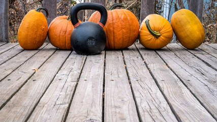 heavy iron kettlebell with a crop of pumpkins on a wooden deck, fall holidays and fitness concept