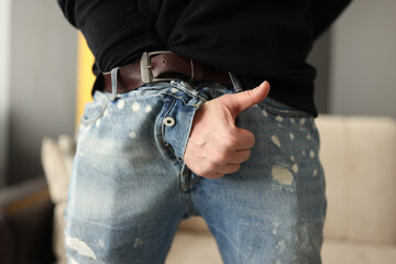 Male hand sticking out of fly of his jeans and showing thumb up close-up. Treatment of sexual dysfunction in men concept