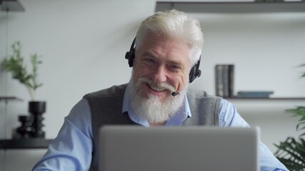 An elderly businessman in a headset having a video conference with a business partner working in an...