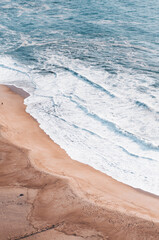 Ocean and beach view from above, shooting from above, blue waves, orange sand. Foam from waves on the shore