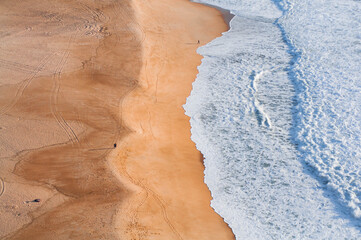 Ocean and beach view from above, shooting from above, blue waves, orange sand. Foam from waves on the shore