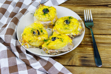 Pieces of baked pork with pineapple, cheese and olive on a wooden table