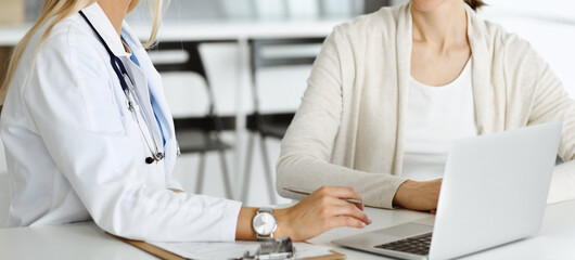 Unknown woman-doctor sitting and communicating with female patient. Physician checks medical history record and exam results, close-up. Healthcare concept