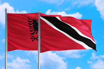 Trinidad And Tobago and Albania national flag waving in the windy deep blue sky. Diplomacy and international relations concept.