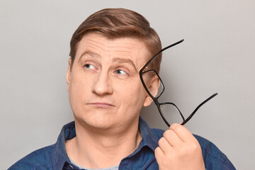 Portrait of thoughtful blond mature man holding glasses in hand