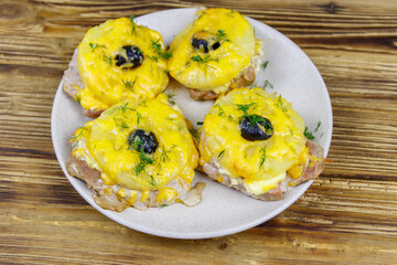 Pieces of baked pork with pineapple, cheese and olive on a wooden table
