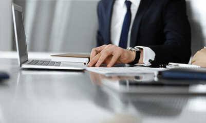 Fototapeta premium Unknown businessmen and woman sitting, using laptop computer and discussing questions at meeting in modern office, close-up