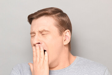 Portrait of sleepy man yawning at large and covering mouth with hand