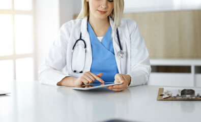 Unknown woman-doctor sitting in sunny clinic and using tablet pc, close-up. Data and best service in medicine