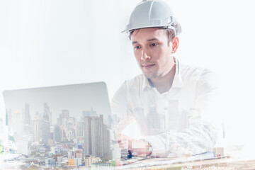 Double exposure of construction engineer wearing hard hat with laptop and view of city.