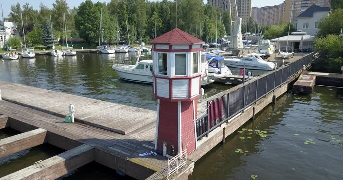 4K high quality calm windless bright summer morning aerial video of Moscow Channel yacht club embankment with wooden lighthouse, green trees, wooden pier, moored anchored boats near Moscow, Russia