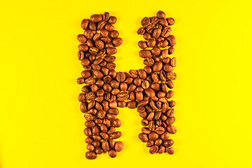 Latin alphabet letters made with coffee beans on yellow background