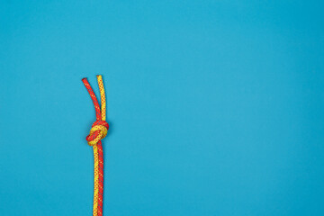 Overhand knot with red and yellow climbing rope on blue background