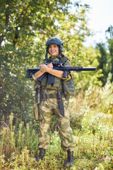 portrait of confident military woman with a gun in forest, hunter female in camouflage suit with a...