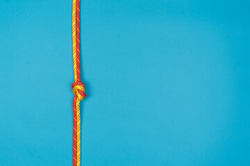 Overhand knot with red and yellow climbing rope on blue background