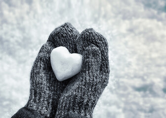 Female hands in knitted mittens with heart of snow in winter day. Love concept. Valentine day background.