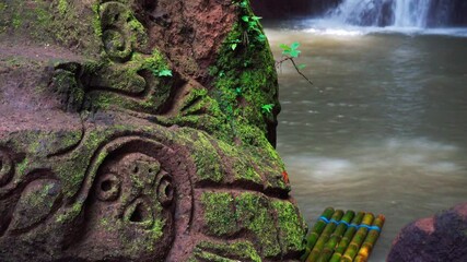 Beautiful waterfall hidden in tropical rainforest jungle with bamboo raft on background scenery stone carving stone in Maya style. 4K Travel in wild nature