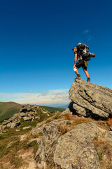 Young man with a backpack standing on top of a mountain and enjoying the view of the valley, the top of the Carpathians Eared stone.